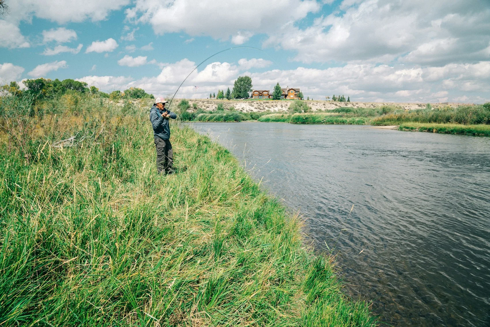 An angler on a grassy riverbank